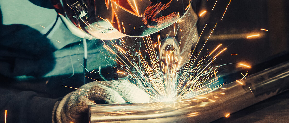 Welder in mask welding metal and sparks metal. Toned image. Welding with sparks close up view Schlagwort(e): weld, welder, welding, spark, steel, metal, worker, mask, eyewear, safety, equipment, factory, man, working, construction, fire, craftsman, workshop, metalwork, engineering, fabrication, flash, flame, gas, hot, industrial, industry, iron, work, toned, colored, light, manual, manufacture, manufacturing, protective, clothing, one, person, gloves, protection, skill, technology, tool, torch, repair, shield, employee, inside, indoor