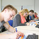 Auszubildende nehmen an einem Seminar teil und schreiben auf Arbeitsblättern, während sie vor einem Computer sitzen. 